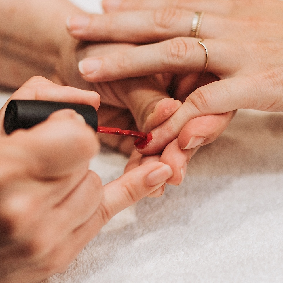 Red polish is applied to the nail on a pinky finger during a manicure